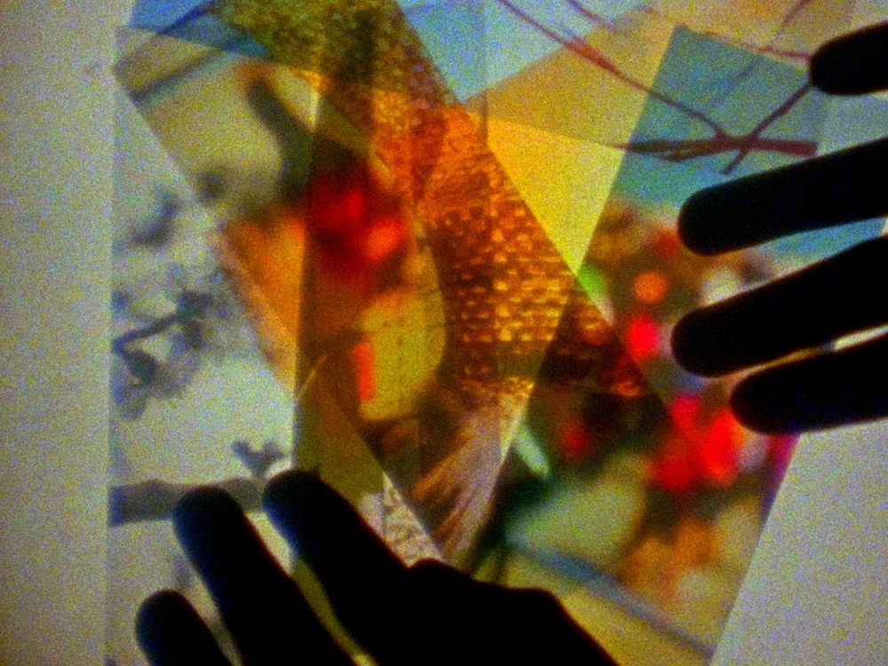 Backlit hands placing various sheets of transparents colorful abstract images overlapping on top of each other creating new colors and patterns.