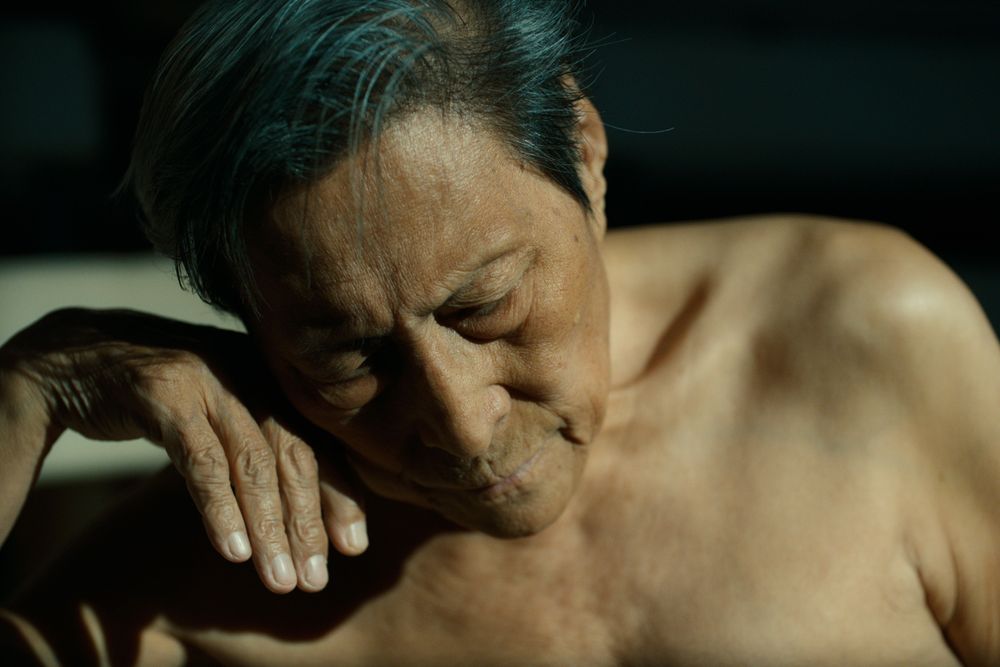 Man, seen from the bust upwards, lit by warm sunlight gazing downwards, his right hand gently supporting his face. 