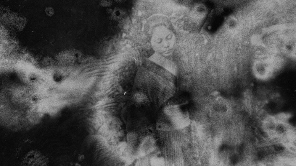 Black and white image with soft, cloud-like textures slightly obscuring the image underneath which shows a woman in traditional attire gazing downwards.