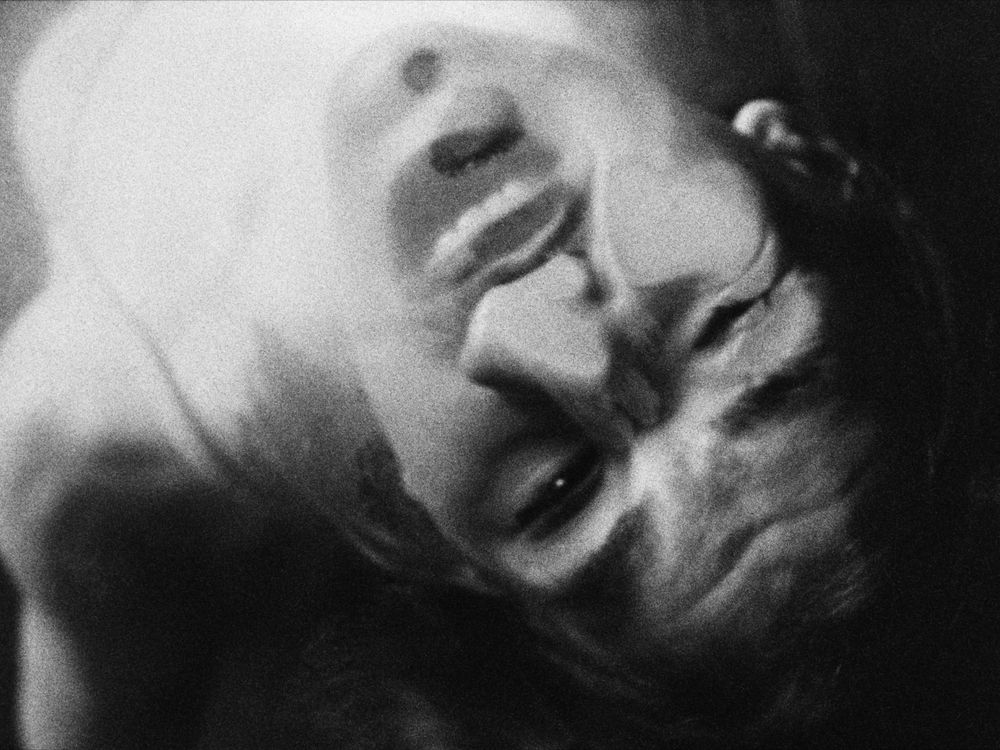 Black and white image of a close-up of a person’s face pressed against a glass surface, their face slightly distorting from the pressure.